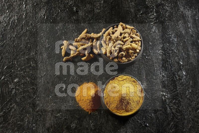 وعاءان من الفخار باللون الأسود، أحدهما ممتلئ ببودرة الكركم والآخر ممتلئ بأصابع كاملة من الكركم المجفف على خلفية سوداء