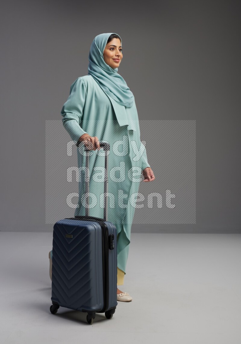 Saudi Woman wearing Abaya standing holding Travel bag on Gray background