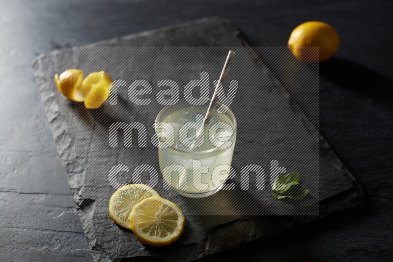 A glass of lemon juice with a straw on black background