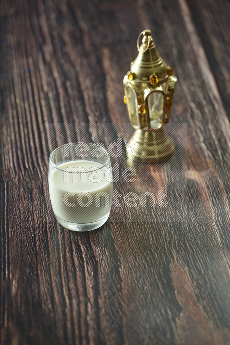 A golden lantern with different drinks, dates, nuts, prayer beads and quran on brown wooden background