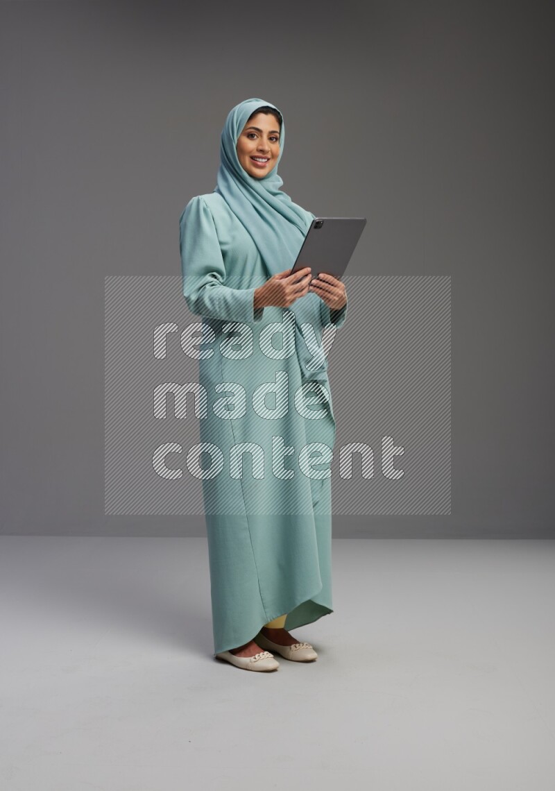 Saudi Woman wearing Abaya standing working on tablet on Gray background