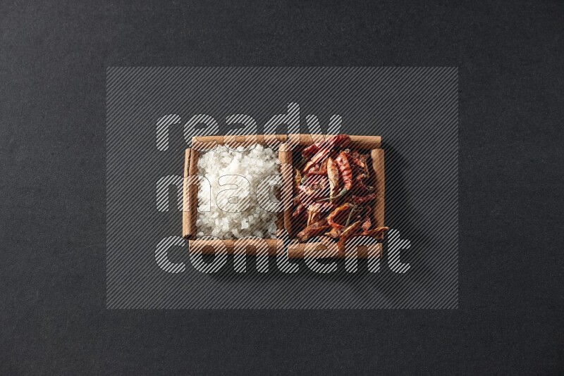 مربعان من أعواد القرفة ممتلئان بالفلفل الحار المجفف والملح الأبيض علي خلفية سوداء