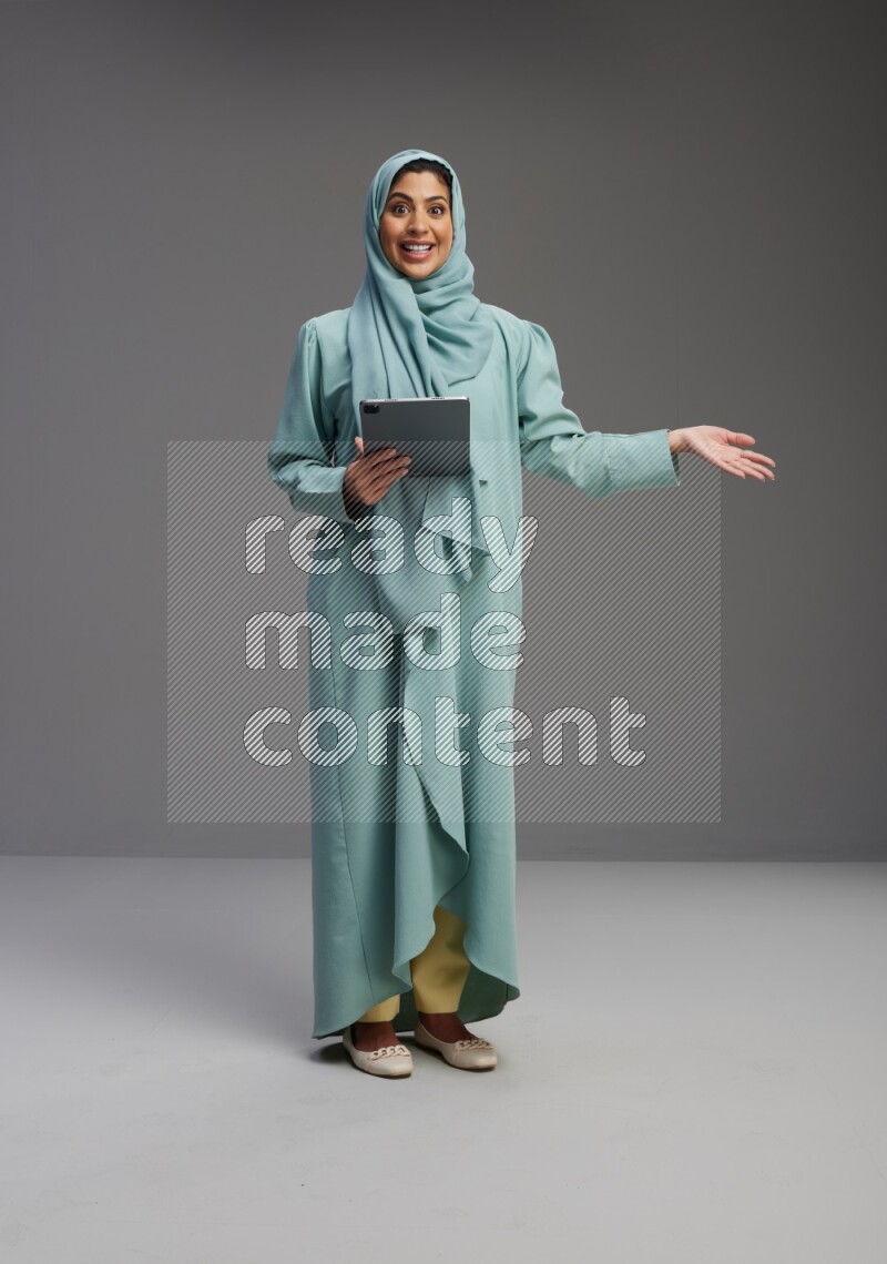 Saudi Woman wearing Abaya standing working on tablet on Gray background