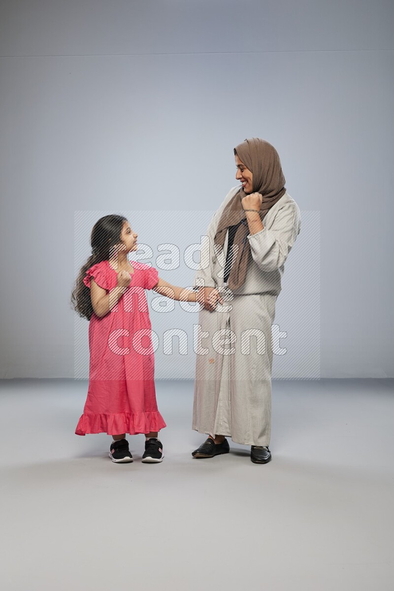 A girl and her mother interacting with the camera on gray background