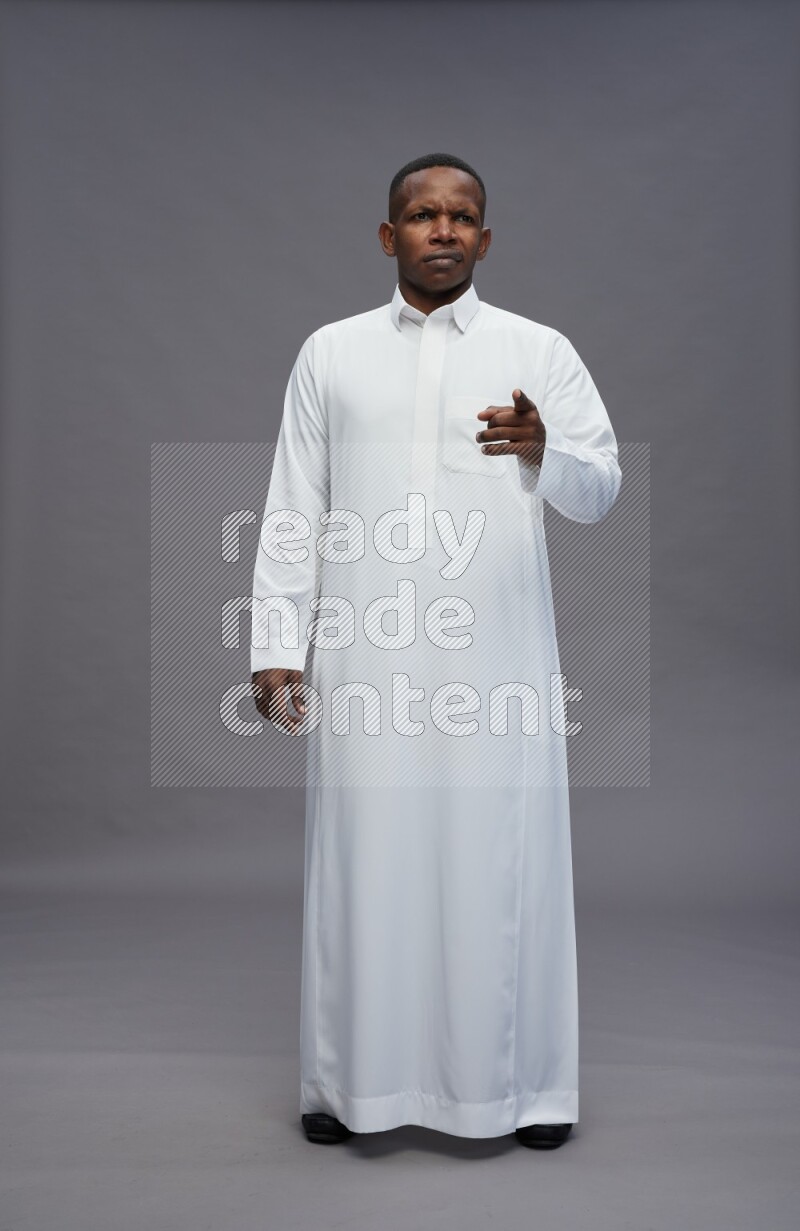 Saudi man wearing thob standing interacting with the camera on gray background