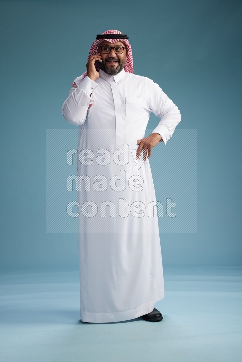 Saudi Man with shimag Standing talking on phone on blue background