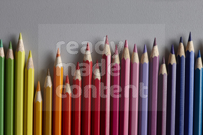 A collection of colored pencils arranged showcasing a gradient of different hues on grey background