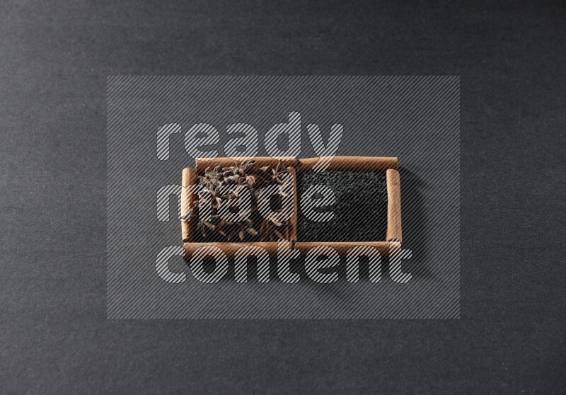 مربعان من أعواد القرفة ممتلئان بحبة البركة السوداء واليانسون النجمي علي خلفية سوداء