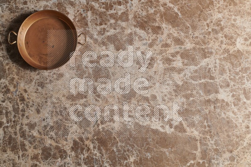 A small copper pan on beige marble background
