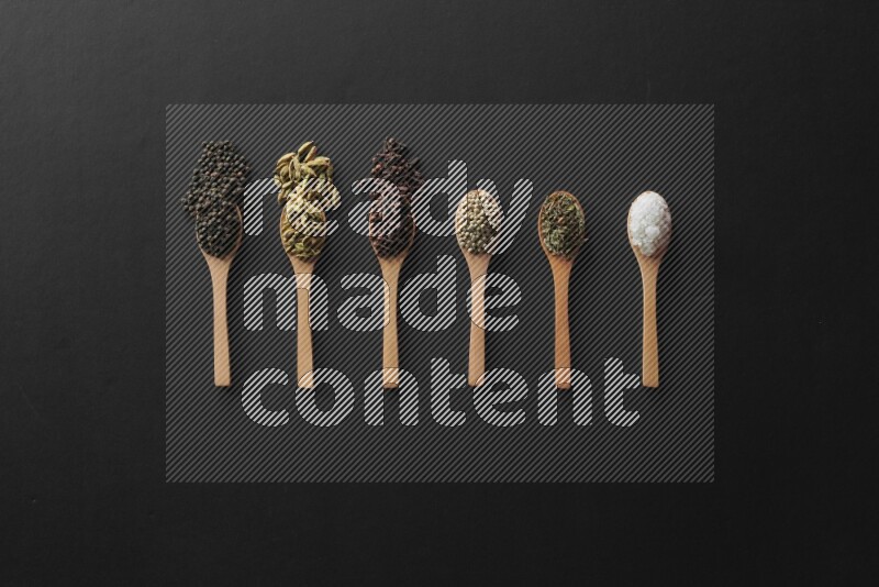 wooden spoons filled with white peppers, cloves, cardamom, salt, black peppers and basil on black flooring