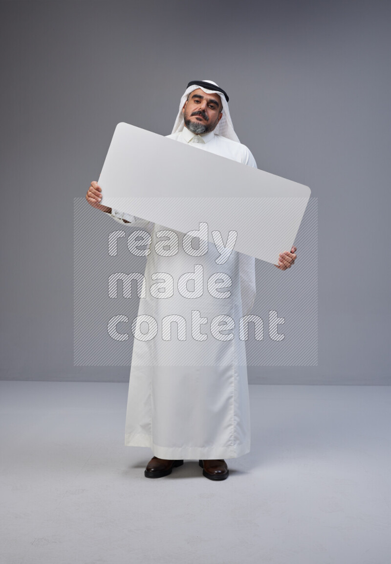 Saudi man Wearing Thob and white Shomag standing holding board on Gray background