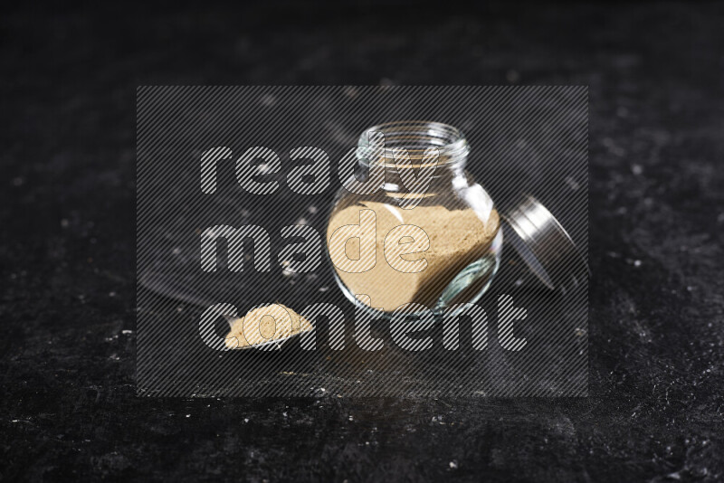 A glass jar full of ground ginger powder on black background