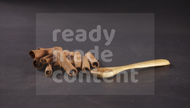 Cinnamon sticks stacked beside a wooden spoon full of cinnamon powder on black background
