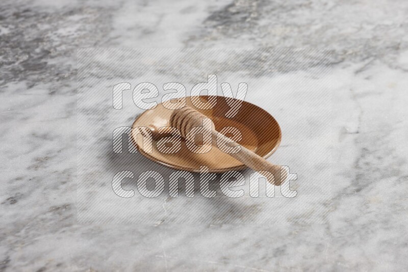 Multicolored pottery plate with wooden honey dipper in it on grey marble background