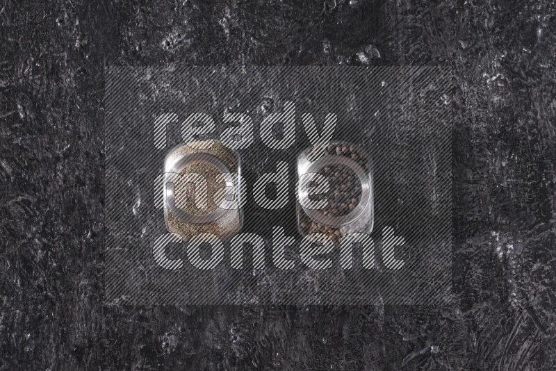 حبوب وبودرة الفلفل الأسود في أوعية زجاجية علي خلفية سوداء