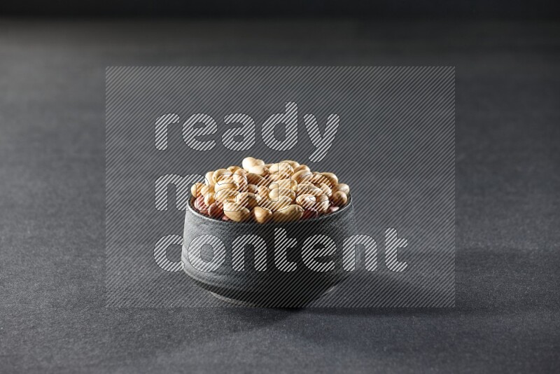 A black pottery bowl full of peeled peanuts on a black background in different angles