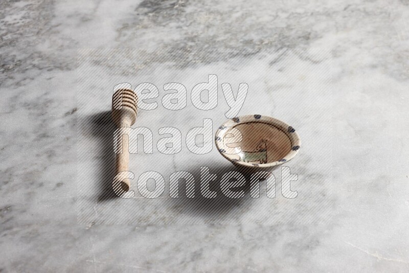 وعاء فخاري مزخرف مع ملعقة عسل خشبية بجانبه على خلفية رخام رمادي