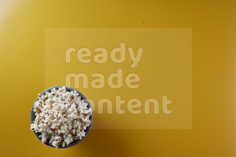 A multicolored pottery bowl full of popcorn on a yellow background in different angles