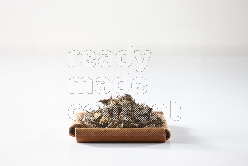 أربعة من أعواد القرفة مكونة شكل مربع بداخلها ريحان مجفف علي خلفية بيضاء