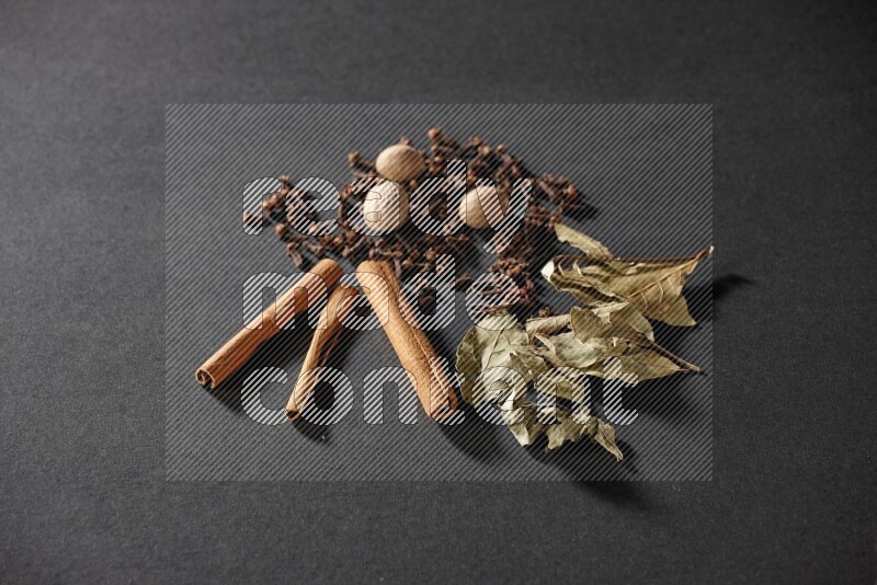 Cloves, ginger, bay laurel and cinnamon sticks on black flooring