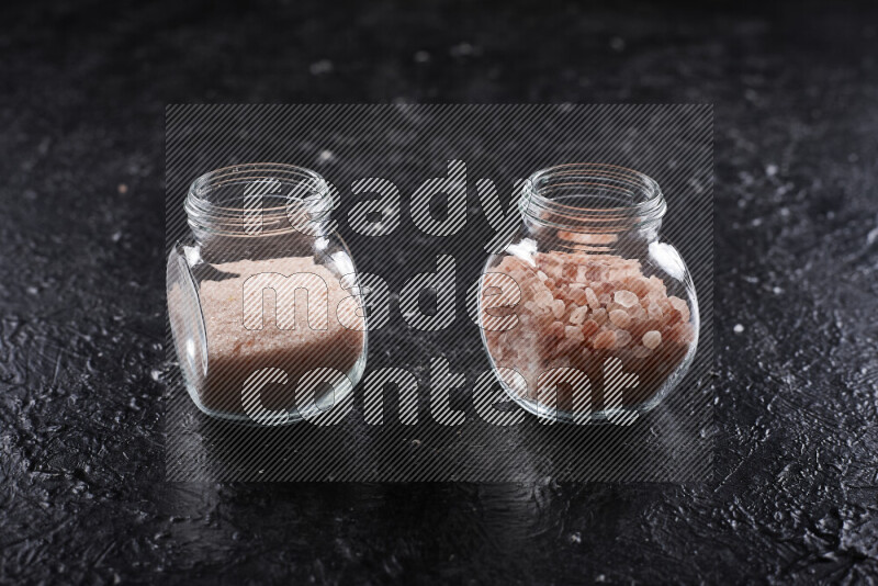 2 glass jars one is filled with fine himalayan salt and the other with coarse himalayan salt on black background