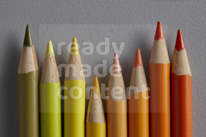 A collection of sharpened colored pencils arranged showcasing a gradient of yellow and orange hues on grey background