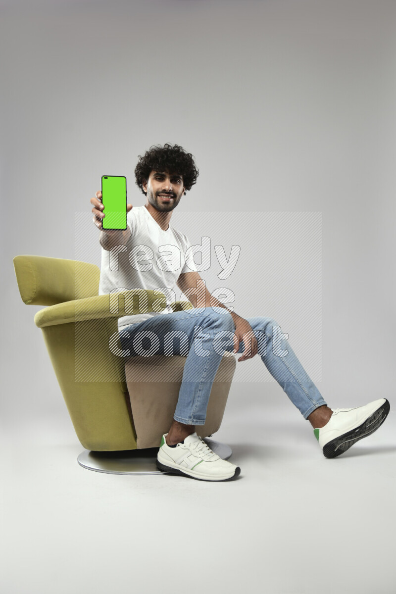 A man wearing casual sitting on a chair showing a phone screen on white background