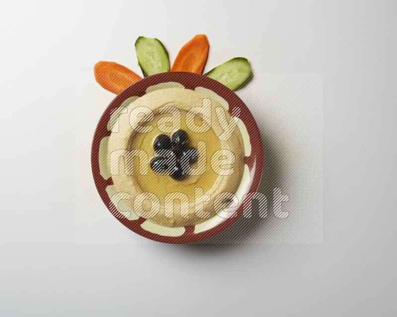 Hummus in a traditional plate garnished with black olives on a white background