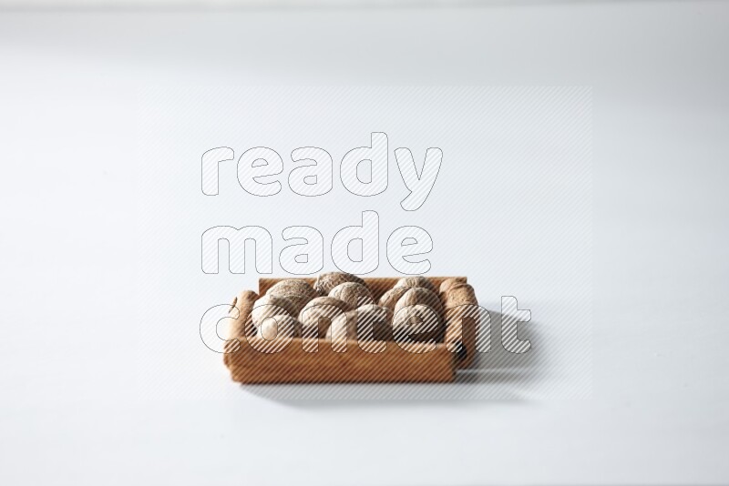 أربعة من أعواد القرفة مكونة شكل مربع بداخلها جوزة الطيب علي خلفية بيضاء