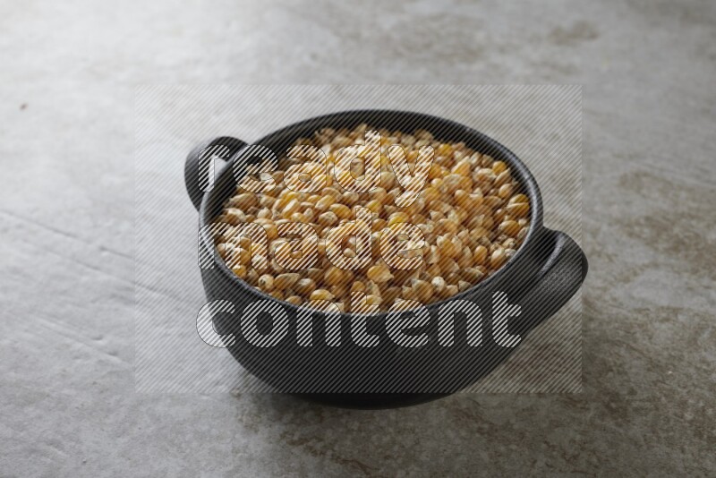 corn kernel in a black handheld ceramic bowl on a grey textured countertop