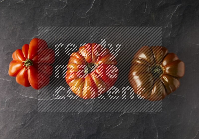 three heirloom tomatoes topview on a black slate background