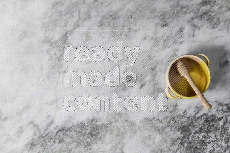 وعاء فخاري متعدد الألوان مع ملعقة عسل خشبية بداخله على خلفية من الرخام الرمادي