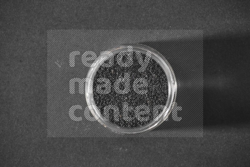 A glass jar full of black seeds on a black flooring