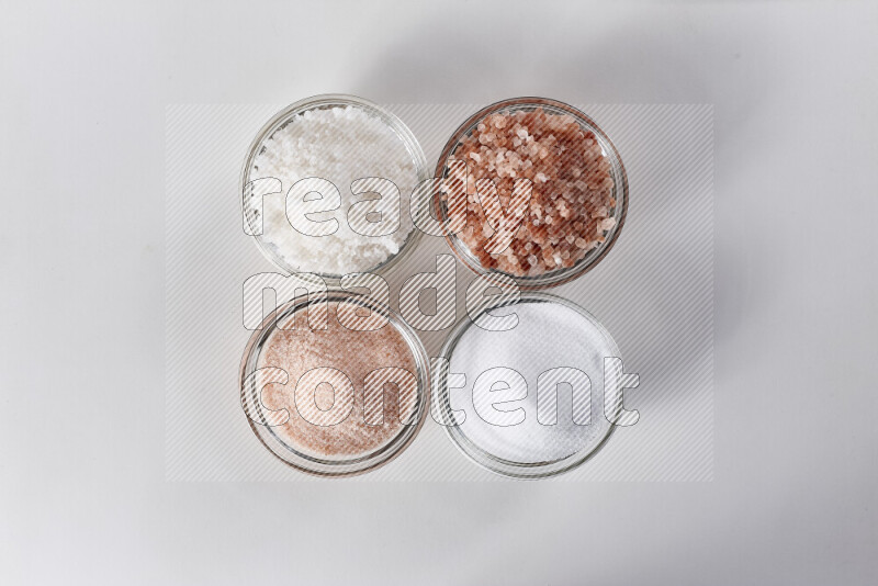 4 glass bowls filled with table salt, coarse sea salt, fine himalayan salt and coarse himalayan salt on white background