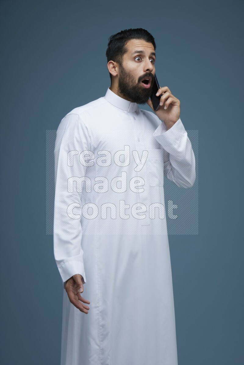 A man having a call on a blue background wearing Saudi Thob