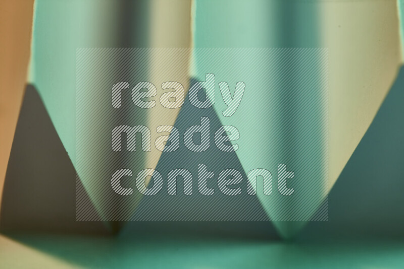 A close-up abstract image showing sharp geometric paper folds in green gradients and warm tones