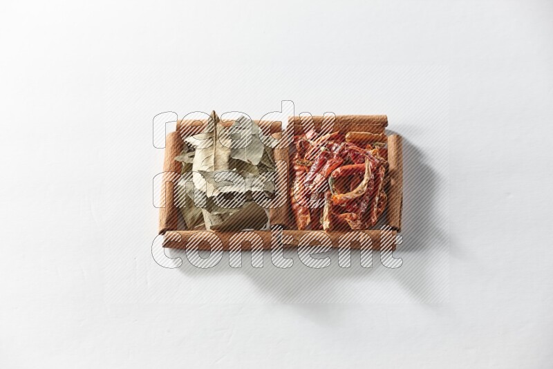 مربعان من أعواد القرفة ممتلئان بالفلفل الحار المجفف وأوراق الغار علي خلفية بيضاء