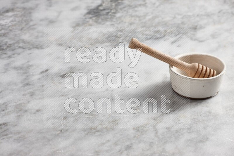 White pottery bowl with wooden honey dipper in it on grey marble background
