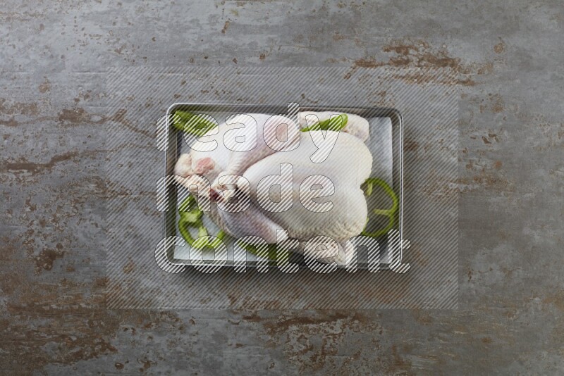 whole Raw chicken on a small oven trey direct on a rustic grey background