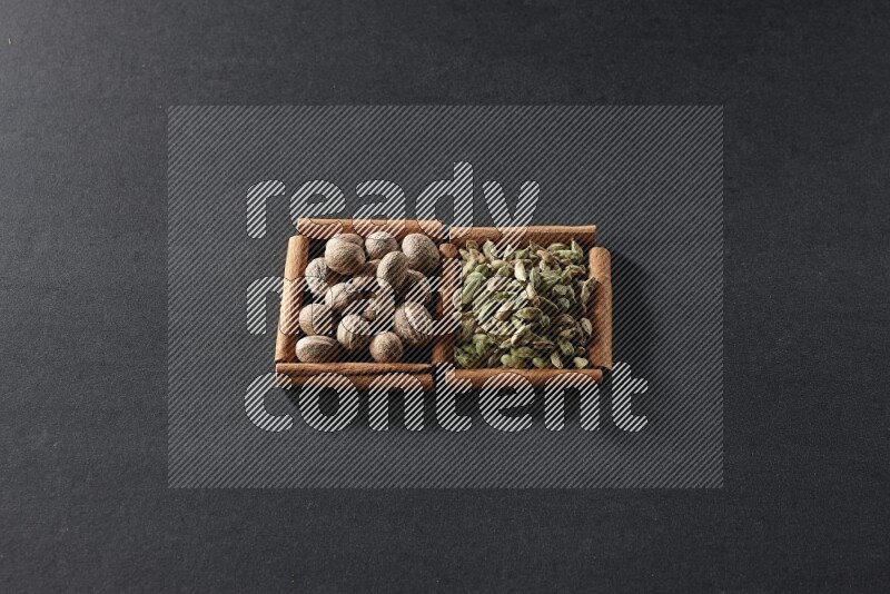 مربعان من أعواد القرفة ممتلئان بجوزة الطيب وحبوب الهيل علي خلفية سوداء