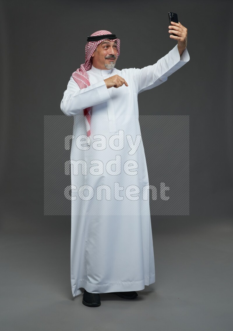 Saudi man with shomag Standing taking selfie on gray background