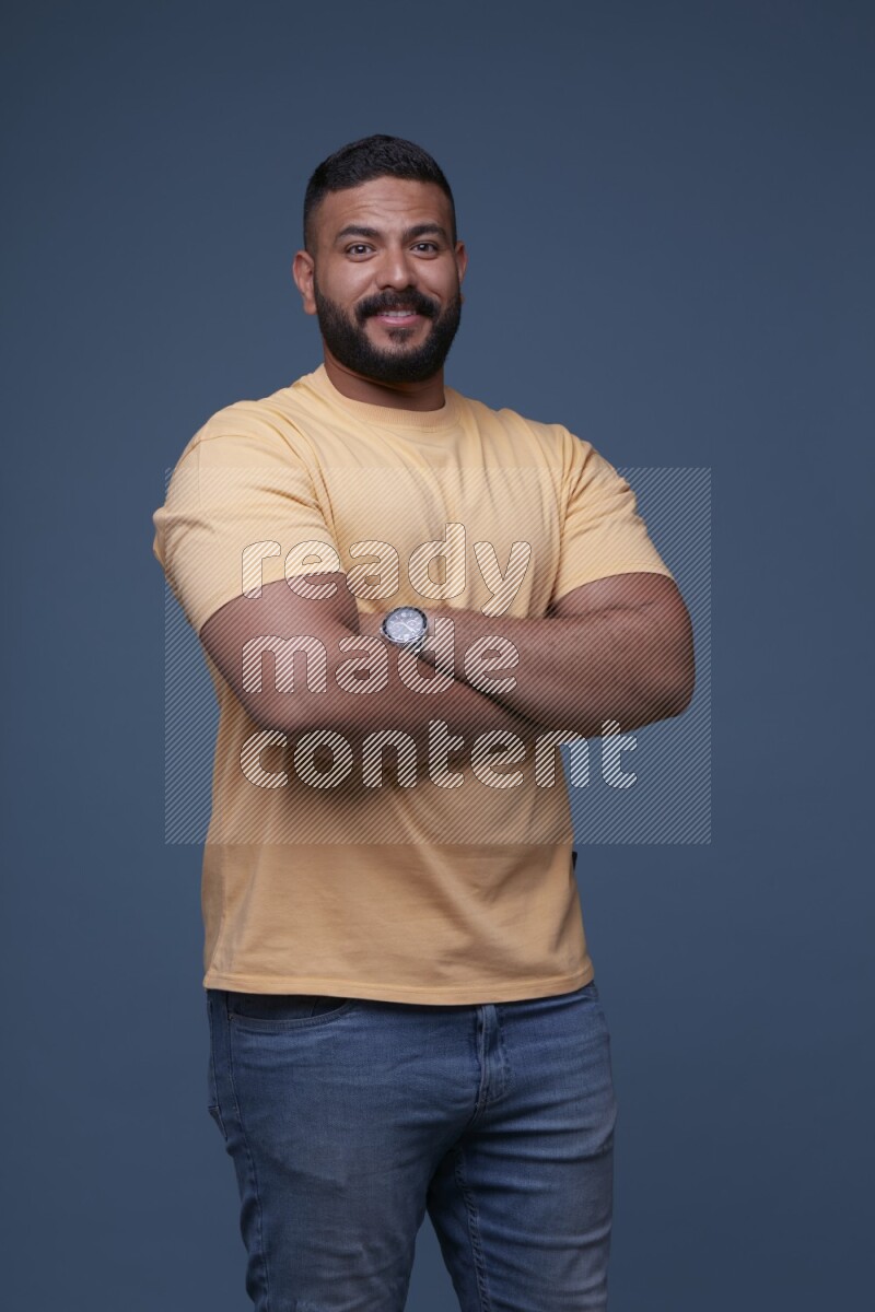A man posing in a blue background wearing a yellow shirt