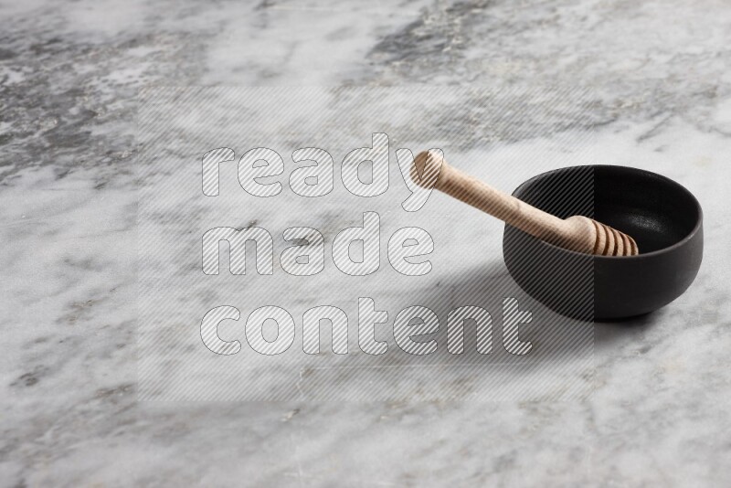 Black pottery bowl with wooden honey dipper in it on grey marble background