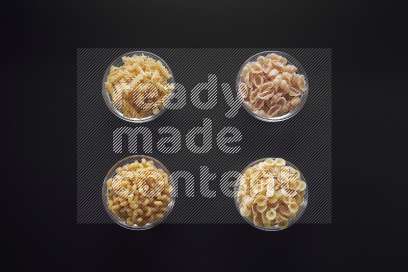 Different pasta types in glass bowls on black background