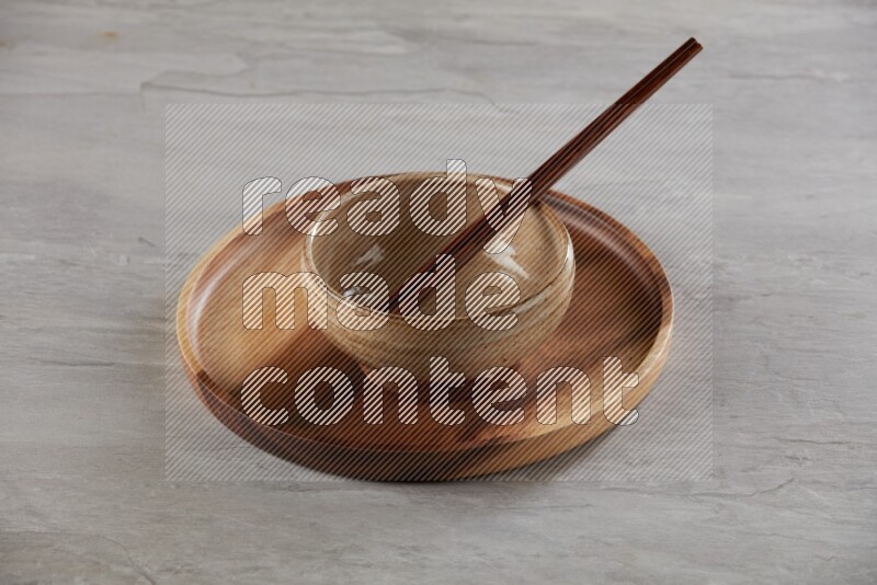 multi color pottery round bowl on top of brown wood round plate and wood chopsticks, on grey textured countertop