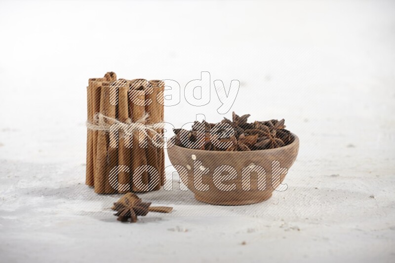 A stacked and bounded cinnamon sticks and a wooden bowl full of star anise on a white background