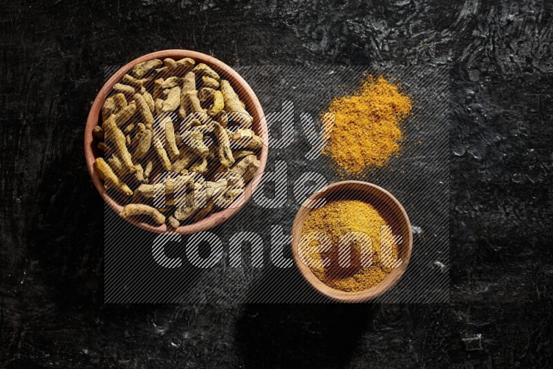 وعاءان خشبيان، أحدهما ممتلئ ببودرة الكركم والآخر بأصابع الكركم المجففة، على خلفية سوداء