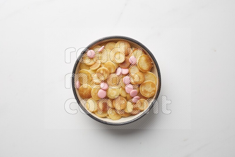 Top-view shot of pink chocolate chips cereal pancakes in a round bowl on white background