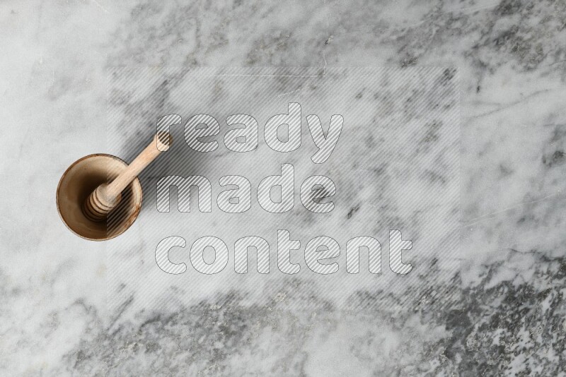 وعاء فخاري بيج مع ملعقة عسل خشبية بداخله على خلفية من الرخام الرمادي