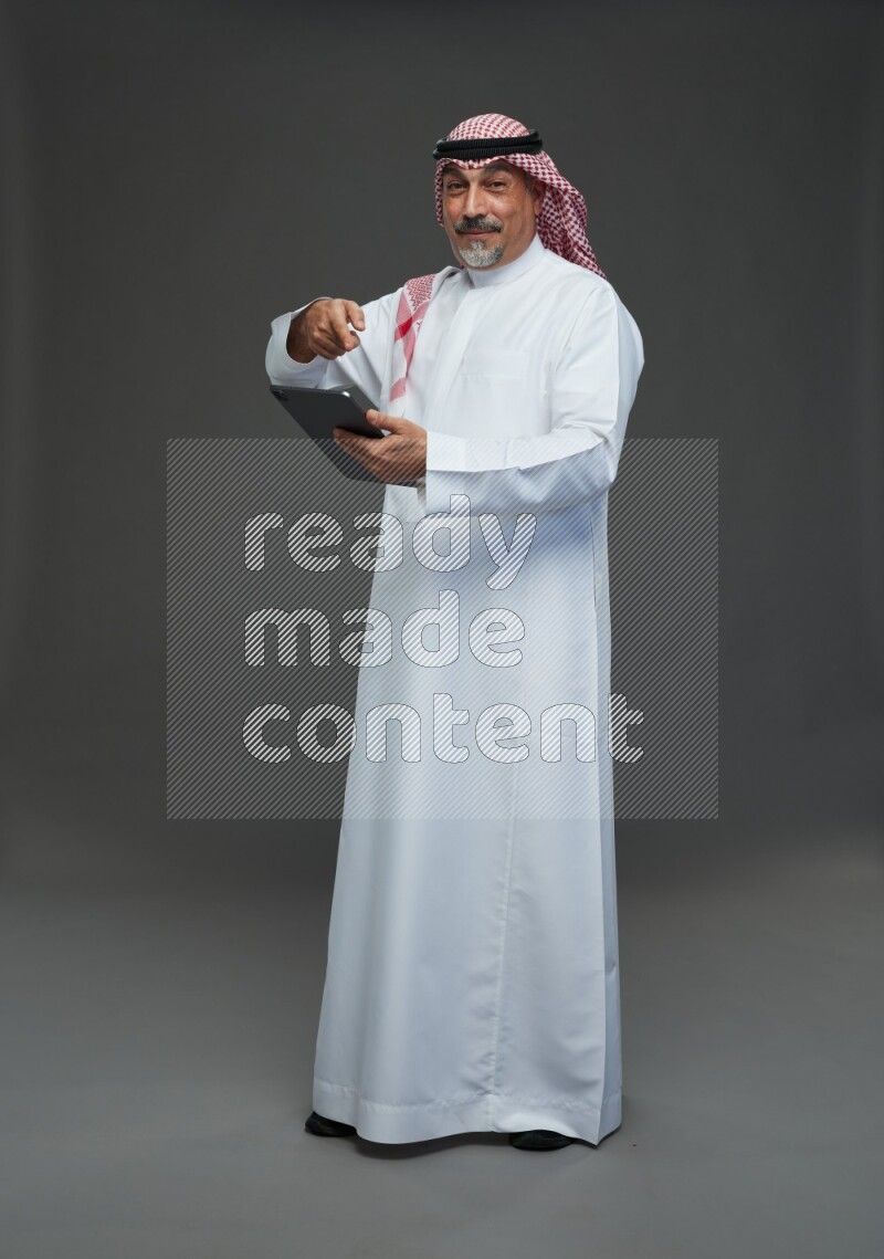 Saudi man with shomag Standing working on tablet on gray background